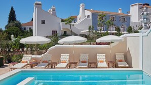 Un espace piscine agrémenté de chaises longues et de parasols, entouré de bâtiments blancs aux toits recouverts de tuiles rouges.