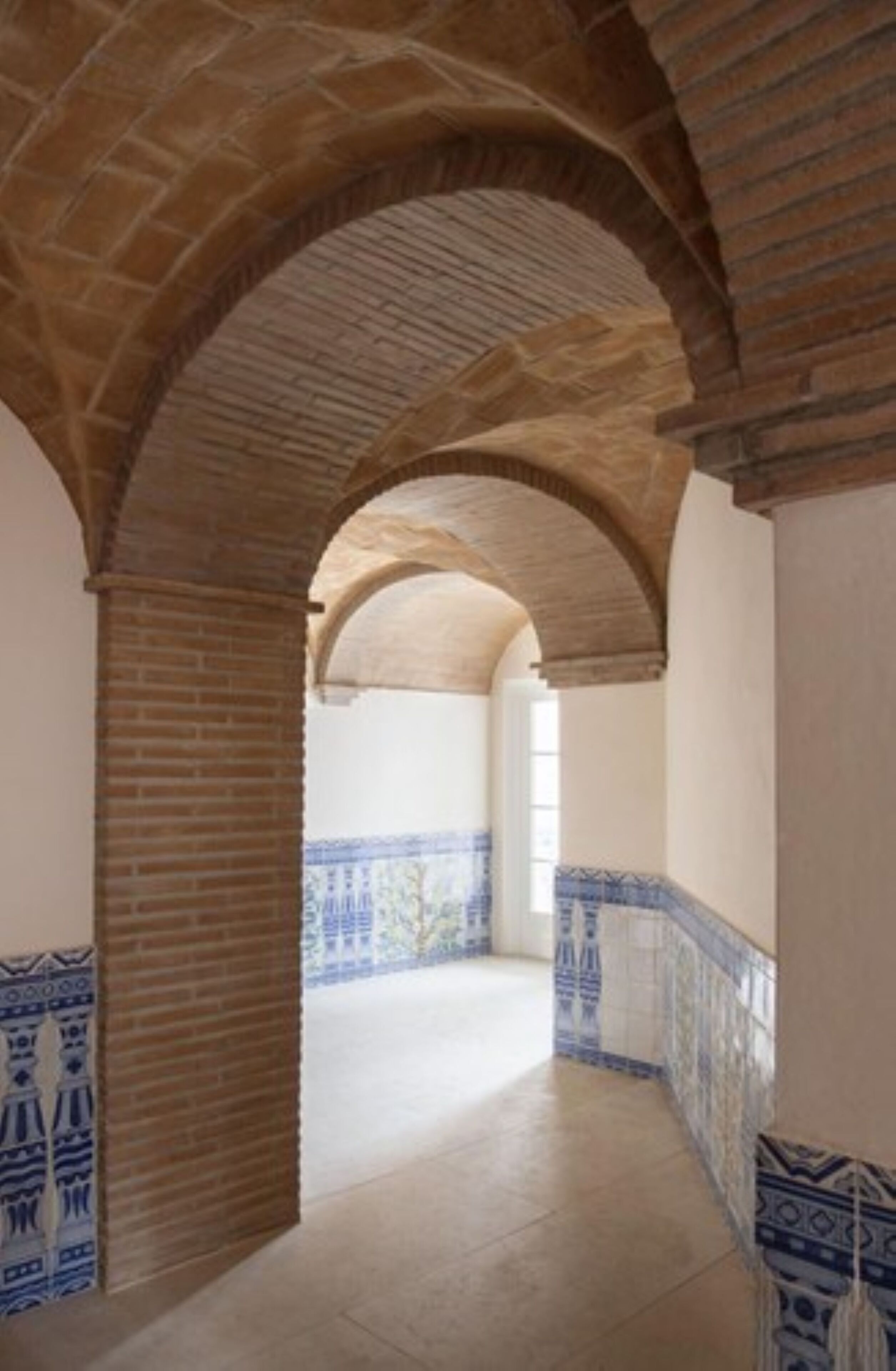 Un passadís interior amb una arcada de maó, parets i terra de rajola.