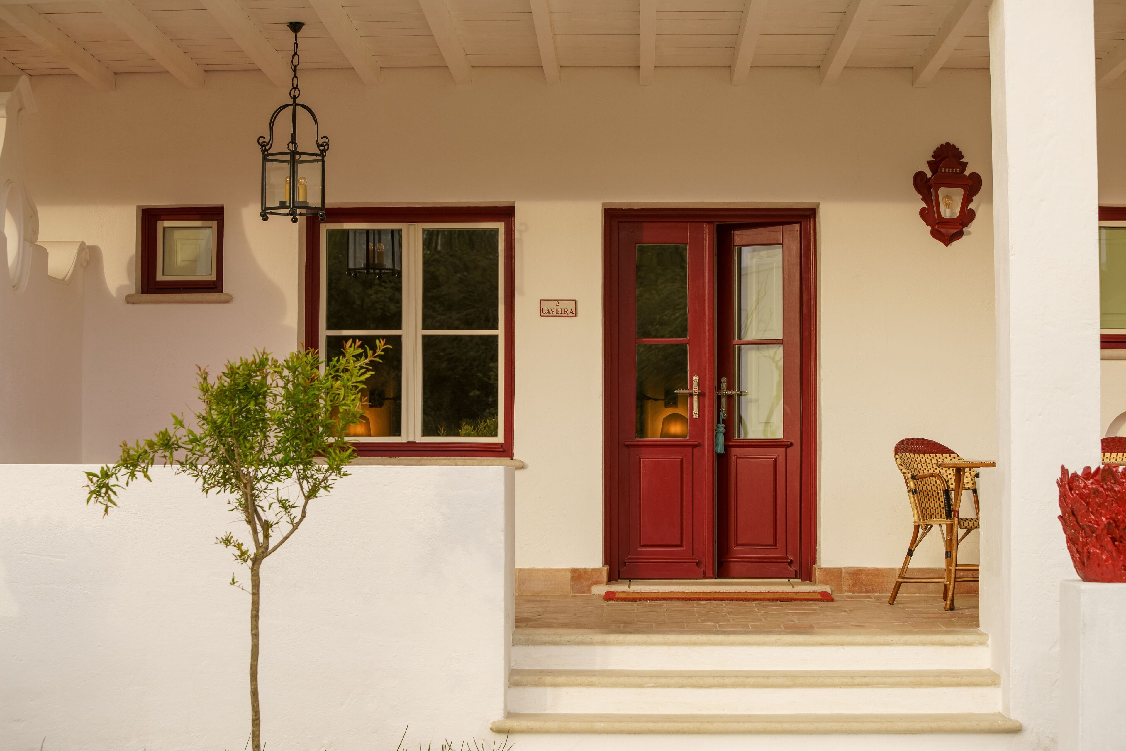 A house with a red door, a small tree in front, and a wicker chair outside.