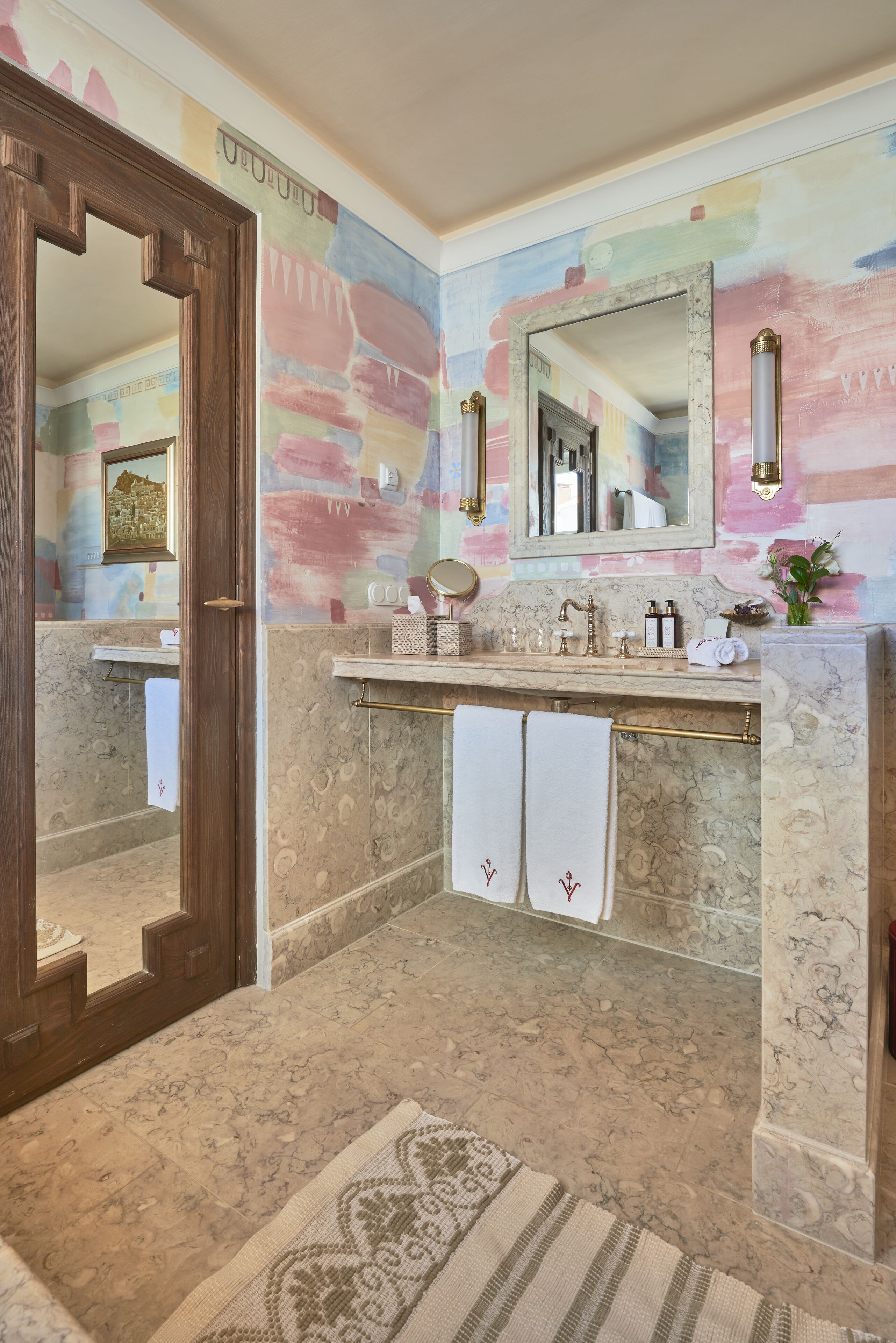 Un baño con piso de mármol, puerta de madera, tocador con espejo y un perchero para toallas.