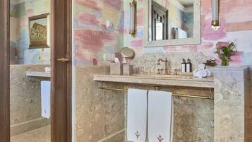 Un baño con piso de mármol, puerta de madera, tocador con espejo y un perchero para toallas.