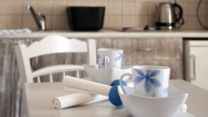 Eine Küche mit einem weißen Tisch, einem weißen Stuhl, einem schwarzen Topf und einer weißen Tasse mit blauem Dekor.