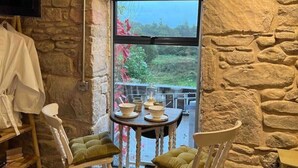 A cozy room with stone walls, a fireplace, a table with chairs, and a TV mounted on the wall. - Charming stone Bothy at Loch Lomond (Muirlands, Arden, Alexandria, Luss,)