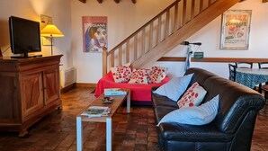A cozy living room with a wooden staircase, a red sofa, a leather couch, and a television on a wooden cabinet. - Charming Cottage: Enclosed Garden, Close to Loire Valley, Sleeps 6 (Beaulieu-sur-Loire)