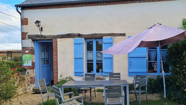 A house with a patio area featuring a table and chairs, a large umbrella, and a sign indicating a city of interest. - Charming Cottage: Enclosed Garden, Close to Loire Valley, Sleeps 6 (Beaulieu-sur-Loire)