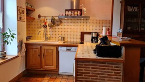 A kitchen with wooden cabinets, a dishwasher, a coffee maker, and a brick backsplash. - Charming Cottage: Enclosed Garden, Close to Loire Valley, Sleeps 6 (Beaulieu-sur-Loire)