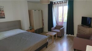 A hotel room with a bed, a small table, a chair, a TV, and a window with curtains.