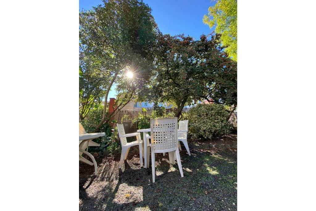 Une terrasse avec une table et des chaises, entourée d’arbres et d’une clôture.