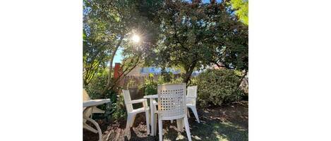 Une terrasse avec une table et des chaises, entourée d’arbres et d’une clôture.