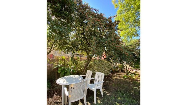 A round table with four chairs in a garden area with trees and a fence in the background.