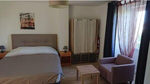 A hotel room with a bed, a chair, a small table, a wardrobe, and a lamp.