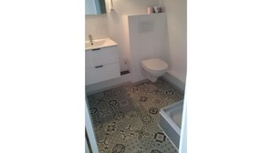 Un baño pequeño con lavamanos blanco, inodoro y suelo de baldosas estampadas.