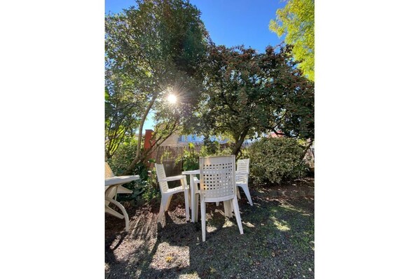 A patio with a table and chairs, surrounded by trees and a fence.
