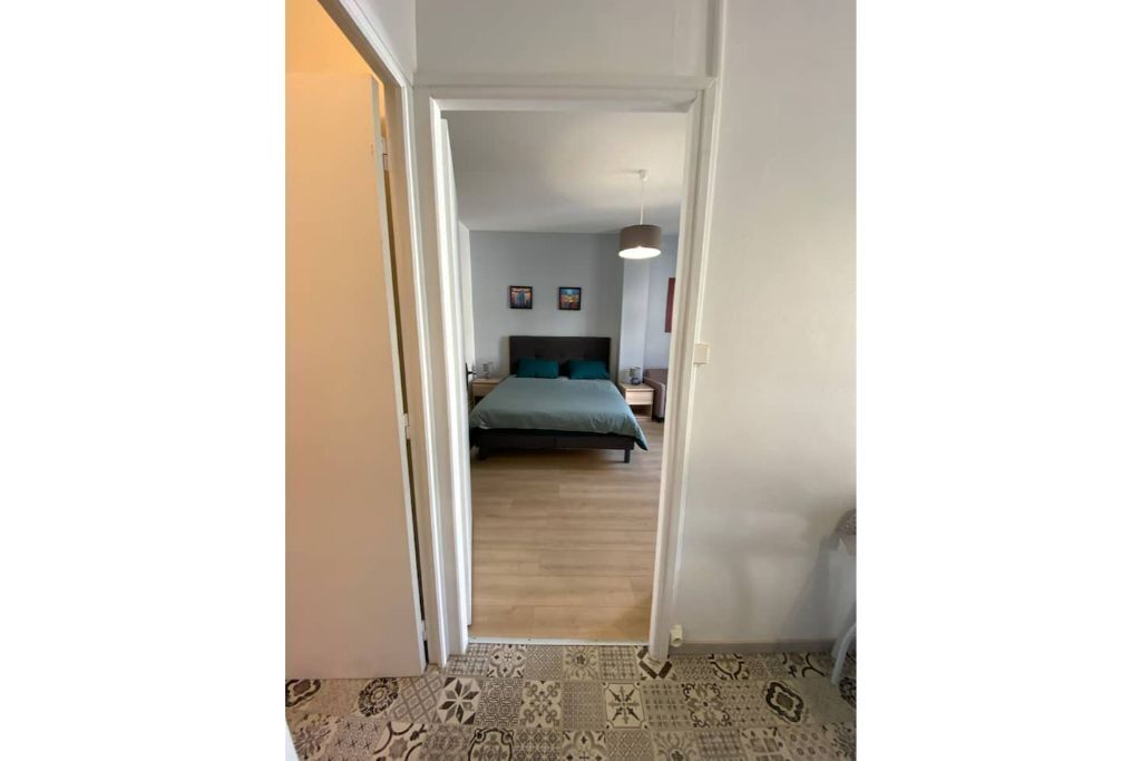 A hallway leading to a bedroom with a bed, a nightstand, and a wall-mounted lamp.