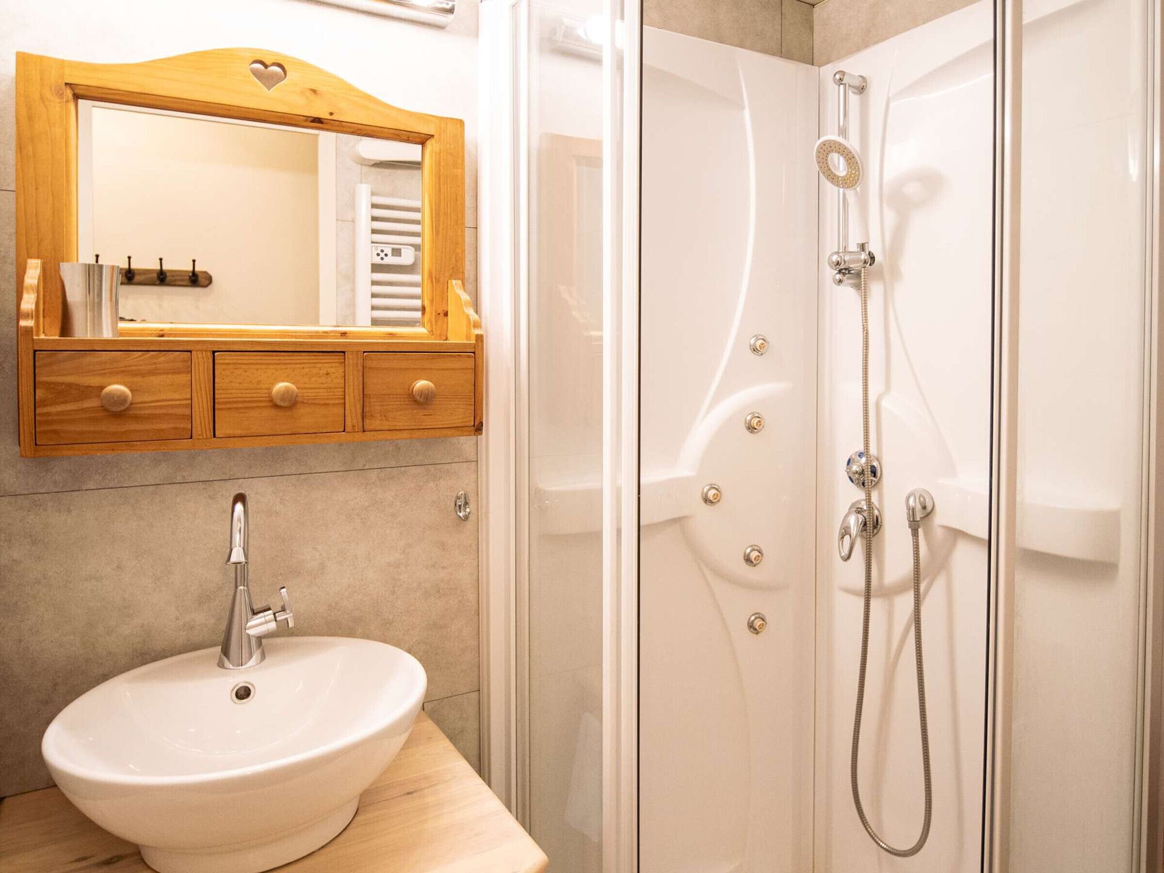 A bathroom with a wooden vanity, a white sink, and a glass-enclosed shower with a handheld showerhead.