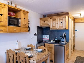 A compact kitchen with wooden cabinets, a microwave, a stove, and a refrigerator. - Cozy Mountain-Style Apartment in Val Thorens - Sleeps 4, Ski-in/Ski-out, Stunning Views (Val Thorens)