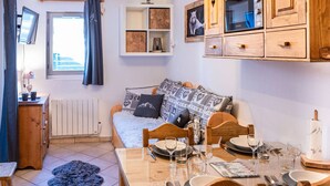 A cozy living room with a sofa, a dining table set for four, and a kitchen area with wooden cabinets and a built-in oven.