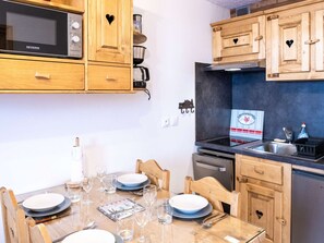 A compact kitchen with wooden cabinets, a microwave, a stove, and a dishwasher. - Cozy Mountain-Style Apartment in Val Thorens - Sleeps 4, Ski-in/Ski-out, Stunning Views (Val Thorens)