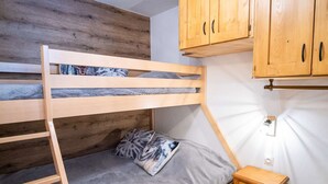 A bunk bed with a wooden headboard, a small bedside table with drawers, and wooden cabinets above the bed.