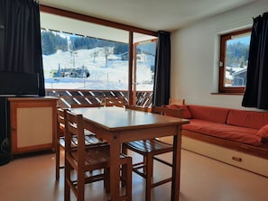 A room with a wooden dining table and chairs, a sofa, and a television.
