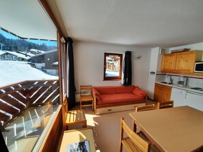 A cozy room with a sofa, wooden chairs, a dining table, and a kitchen area with wooden cabinets and a microwave.