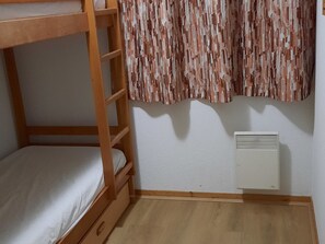 A bunk bed room with a wooden ladder, a white mattress, a small wooden drawer, and a radiator on the wall.