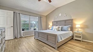 A bedroom with a large bed, a nightstand, a window with curtains, and a ceiling fan.
