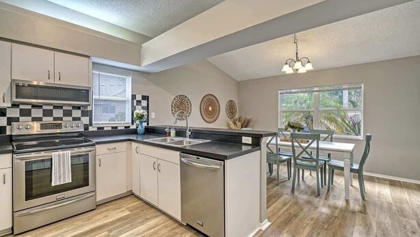 A modern kitchen with stainless steel appliances, a central island, and a dining area with a view of the outdoors.