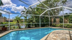 A swimming pool with a glass enclosure, surrounded by lush greenery and palm trees.