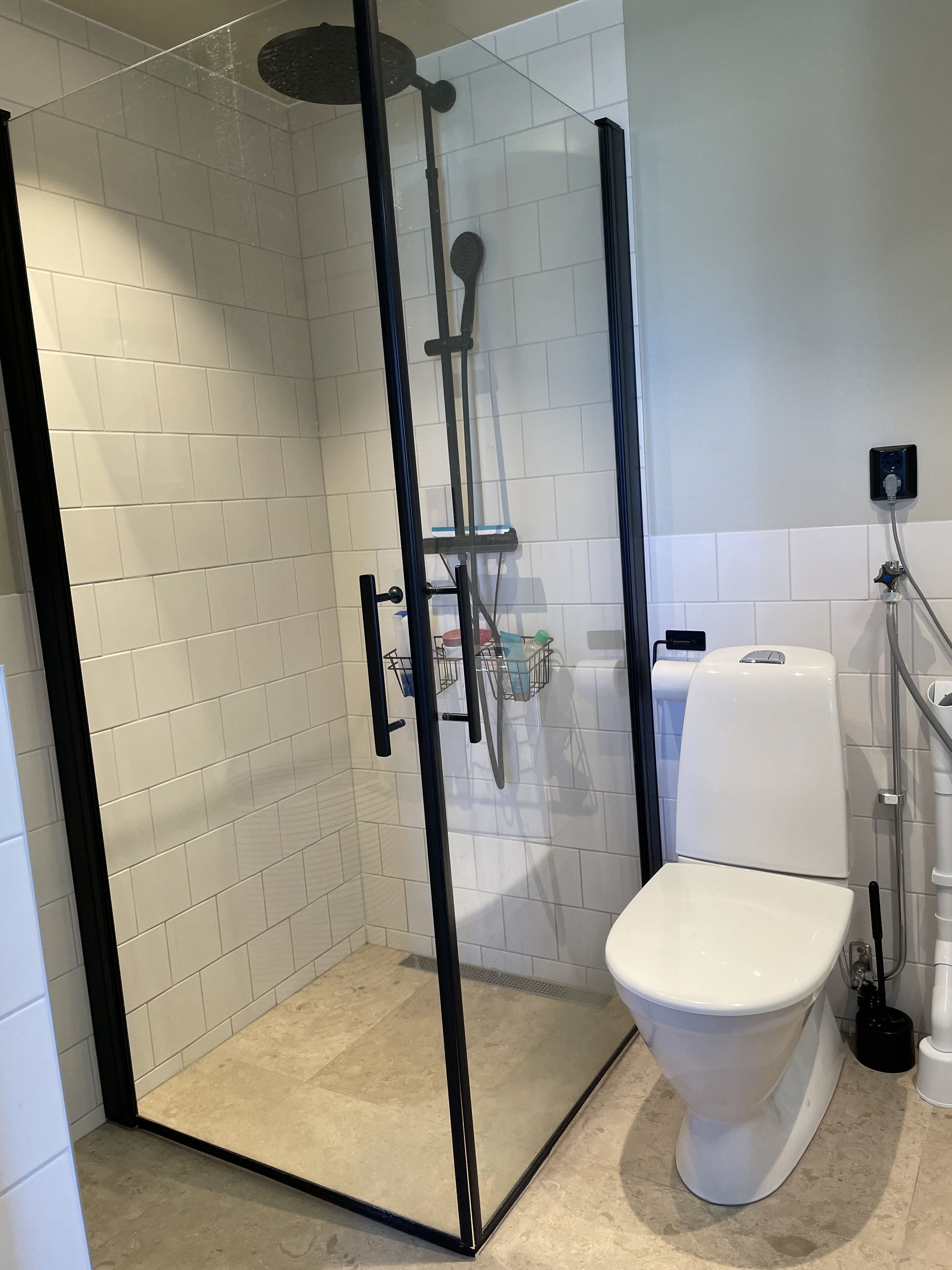 Une salle de bain moderne avec une douche à parois de verre, des murs recouverts de carreaux blancs et des toilettes blanches.