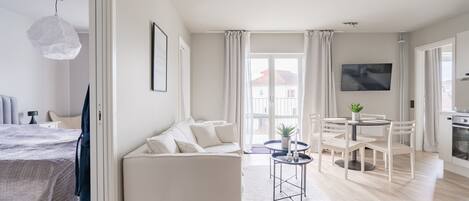 A modern, well-lit living room with a sofa, dining table, and a TV mounted on the wall.