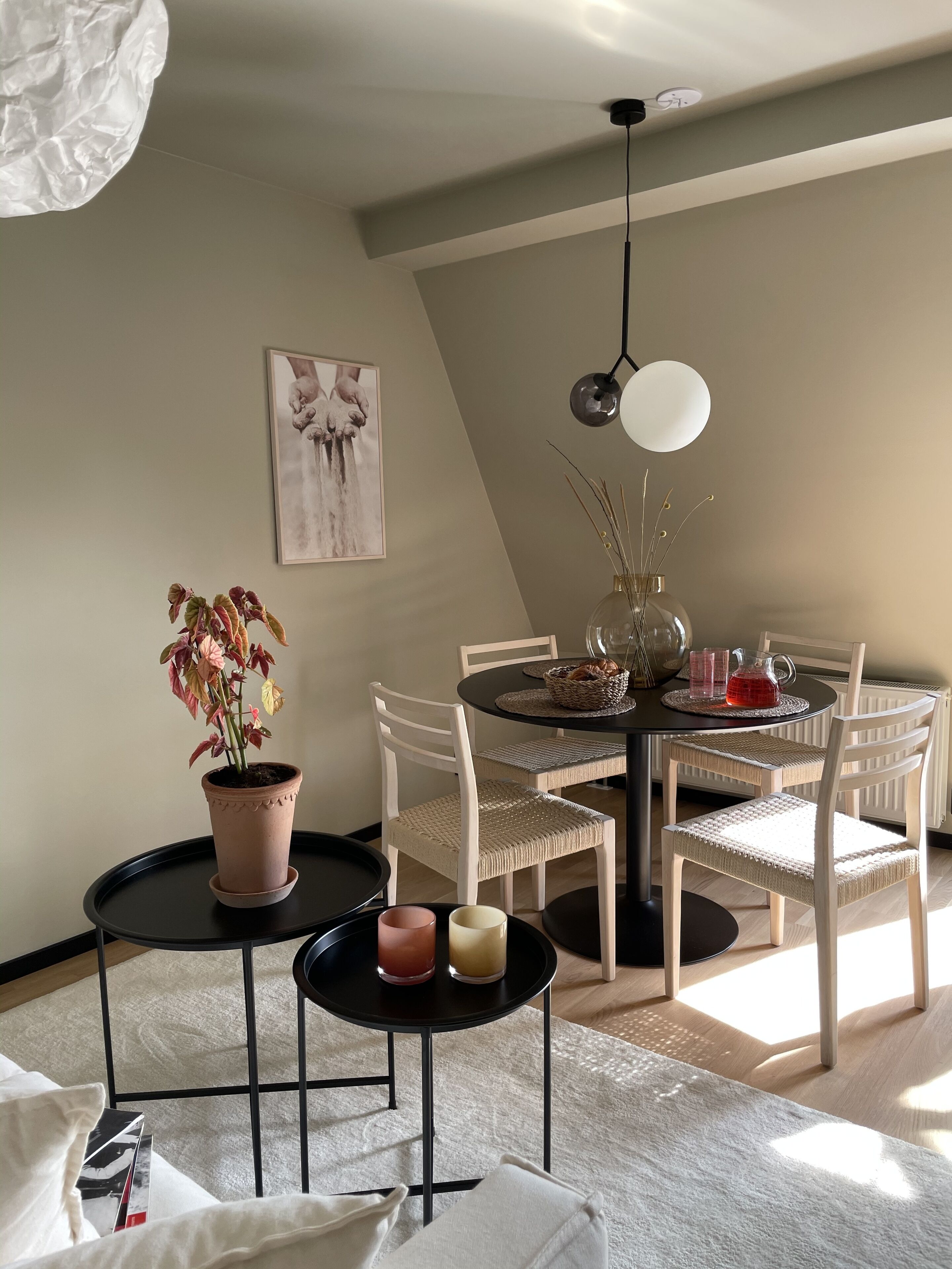 A dining area with a round table, chairs, a potted plant, and a hanging light fixture.