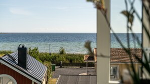 Vista costera desde una ventana con vistas a la playa, con un edificio y una valla en primer plano.