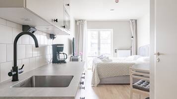 A modern kitchen with a built-in sink and a bed with a bedside table in the adjacent room.