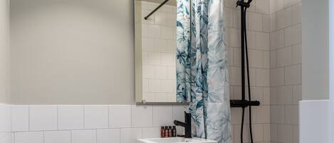 A bathroom with a toilet, sink, mirror, shower, and a towel rack.