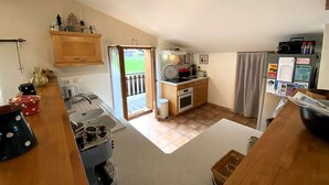 Eine kompakte Küche mit Herd, Spüle und kleinem Kühlschrank. Eine Schiebetür führt zu einem Balkon.