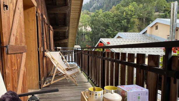 Eine Holzterrasse mit zwei Liegestühlen, einem kleinen Tisch und einer Holzkiste mit Gegenständen.