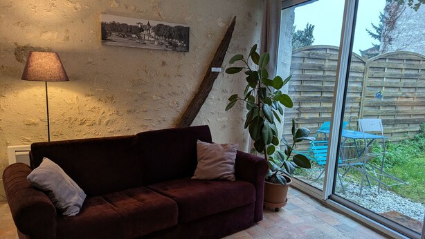 Ein gemütliches Wohnzimmer mit einem dunkelroten Sofa, einer Lampe, einem Topfpflanzen und einem großen Fenster mit Blick auf einen Holzzaun und Grünflächen.