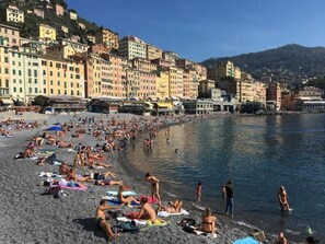 Une plage bondée où les gens se prélassent au soleil et se baignent, entourée d’immeubles aux couleurs vives.