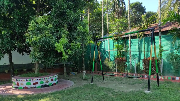 A circular outdoor area with a swing set, surrounded by greenery and a decorative wall.