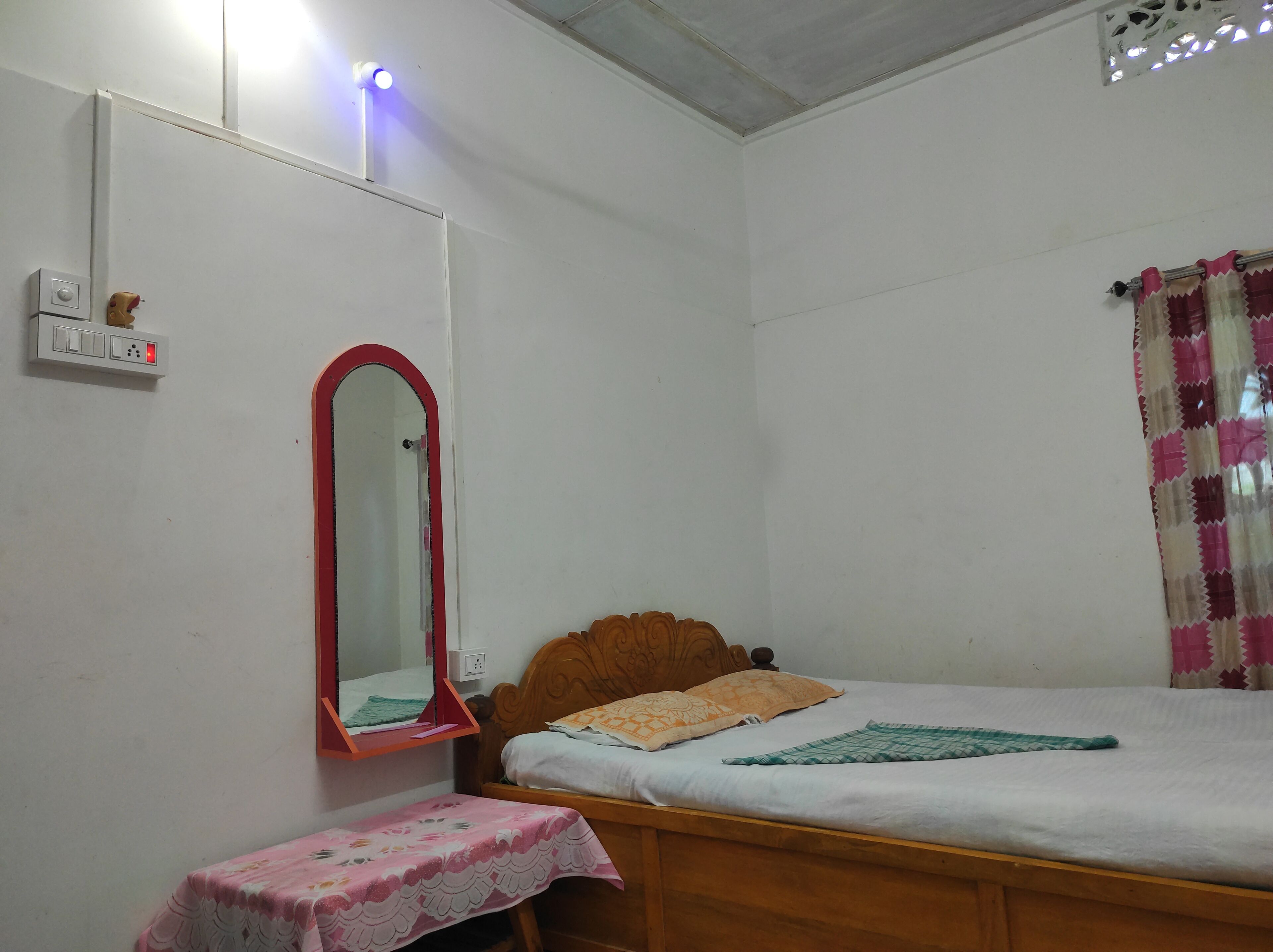 Une petite pièce simple, avec un lit simple, une table de chevet, un miroir et une prise électrique au mur.