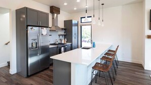 A modern kitchen with a stainless steel refrigerator, a gas stove, and a large island with bar stools. - New 3 story home - Walking distance to the Milwaukee Trail and Good Food Store (Missoula)