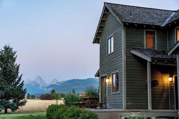 Een huis met twee verdiepingen, uitzicht op een berg, een houten terras en een keurig onderhouden gazon.