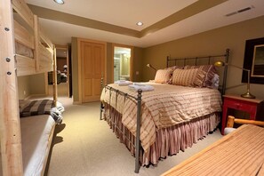 Een slaapkamer met een stapelbed, een eenpersoonsbed, een houten bureau en een stoel.