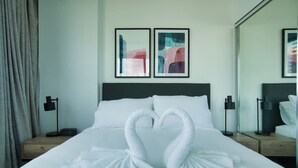 Een hotelkamer met een bed, twee kunstwerken in lijsten boven de hoofdeinde, en een spiegel aan de muur.