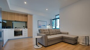 Een moderne woonruimte met een keuken, een grijze modulaire bank en een kleine ronde tafel.