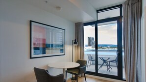Een moderne kamer met een ronde tafel, twee stoelen, een lijst met een abstract schilderij en een groot raam met gordijnen.