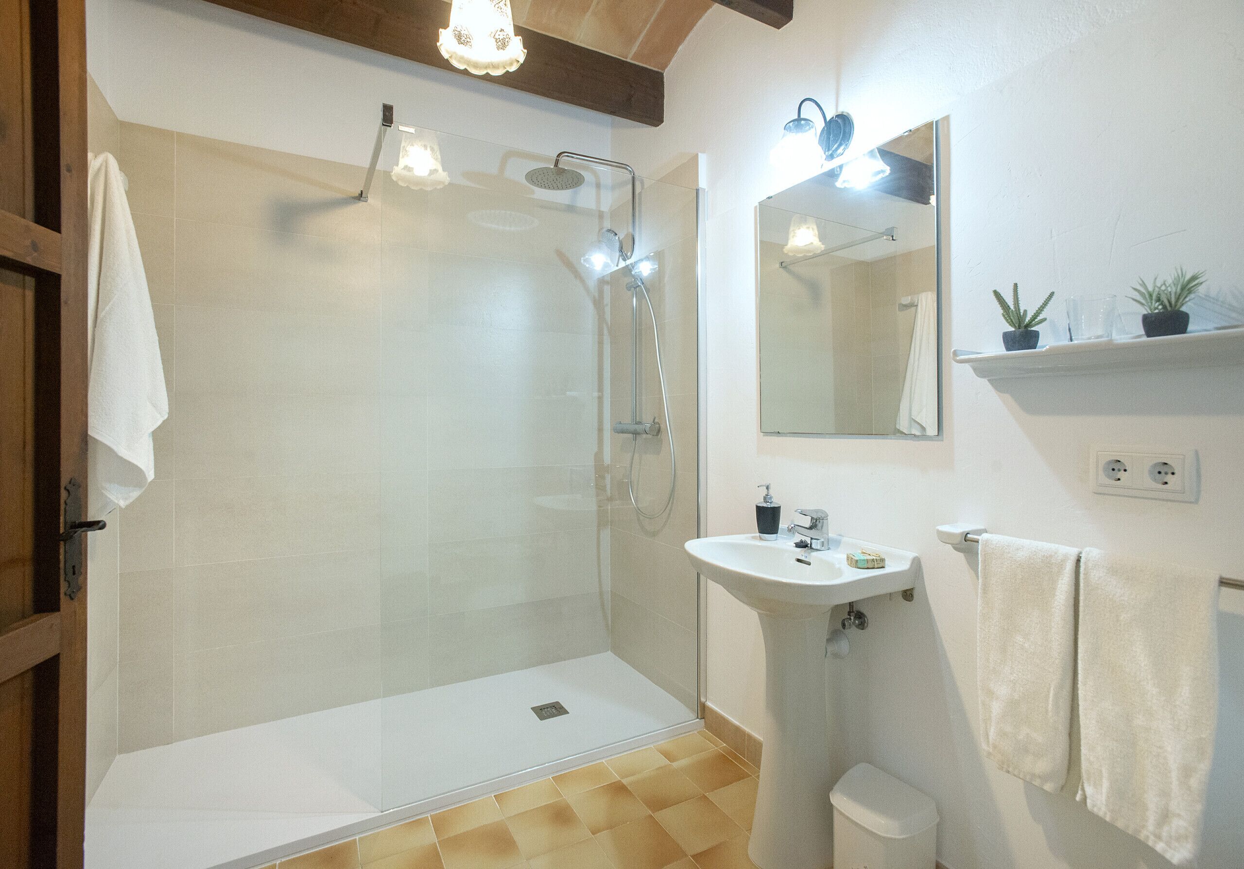 Une salle de bain moderne avec une douche à parois de verre, un lavabo sur colonne et un miroir au-dessus du lavabo.