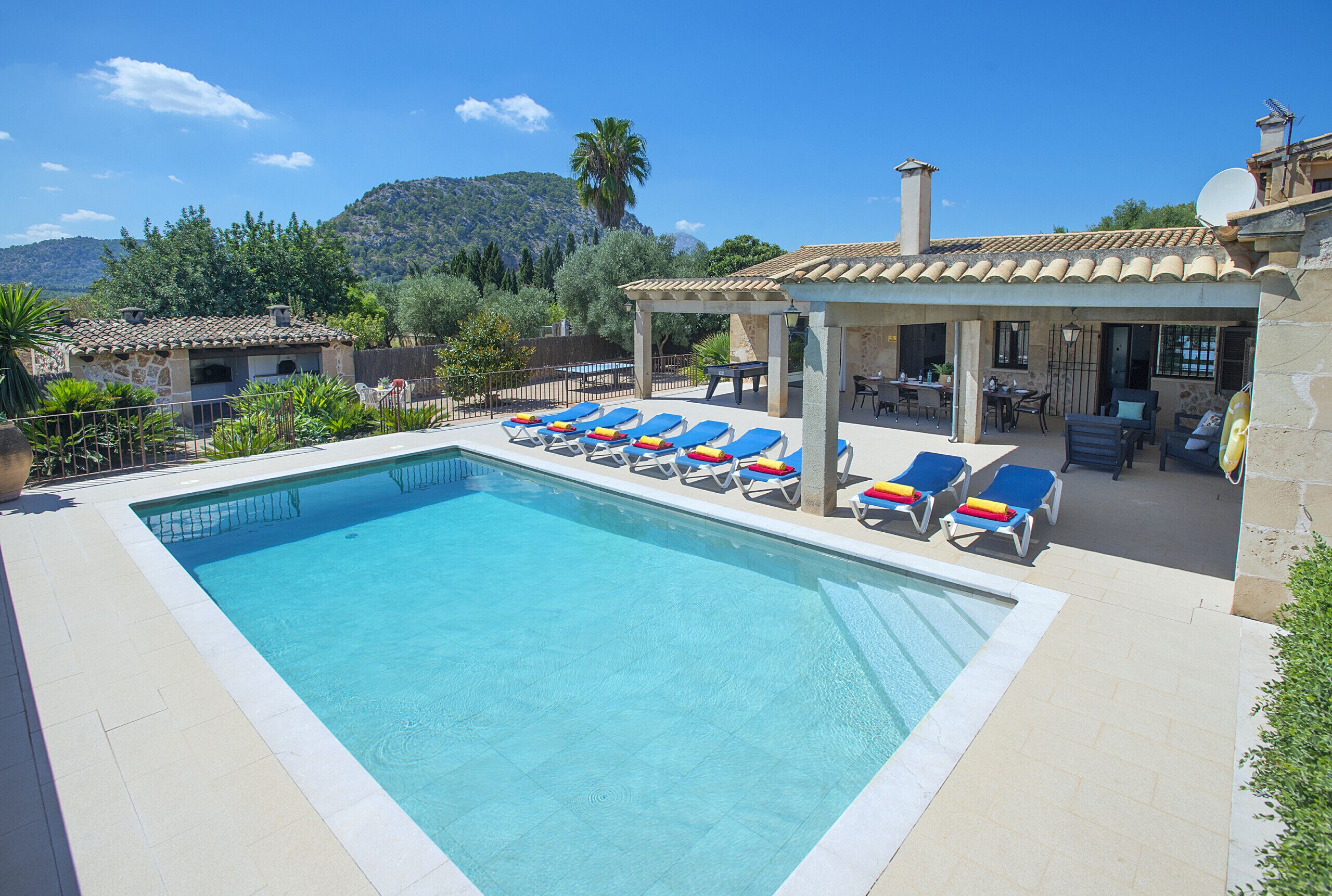 Ein Swimmingpool mit blauen Liegestühlen und einer überdachten Terrassenanlage.