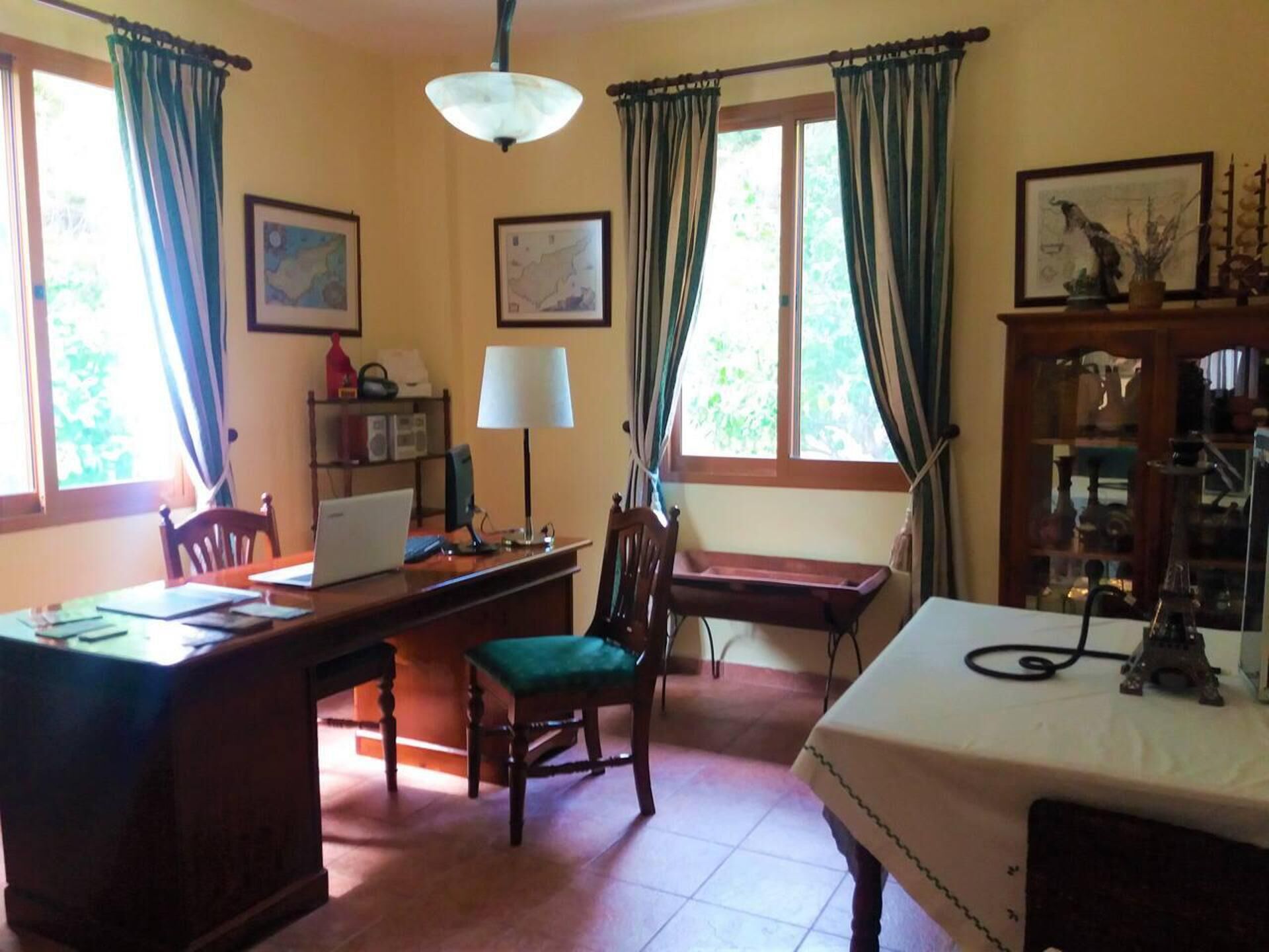 Une pièce comprenant un bureau, une chaise, une lampe et un lit. Il y a deux fenêtres avec des rideaux, une carte accrochée au mur et une étagère avec des objets décoratifs.